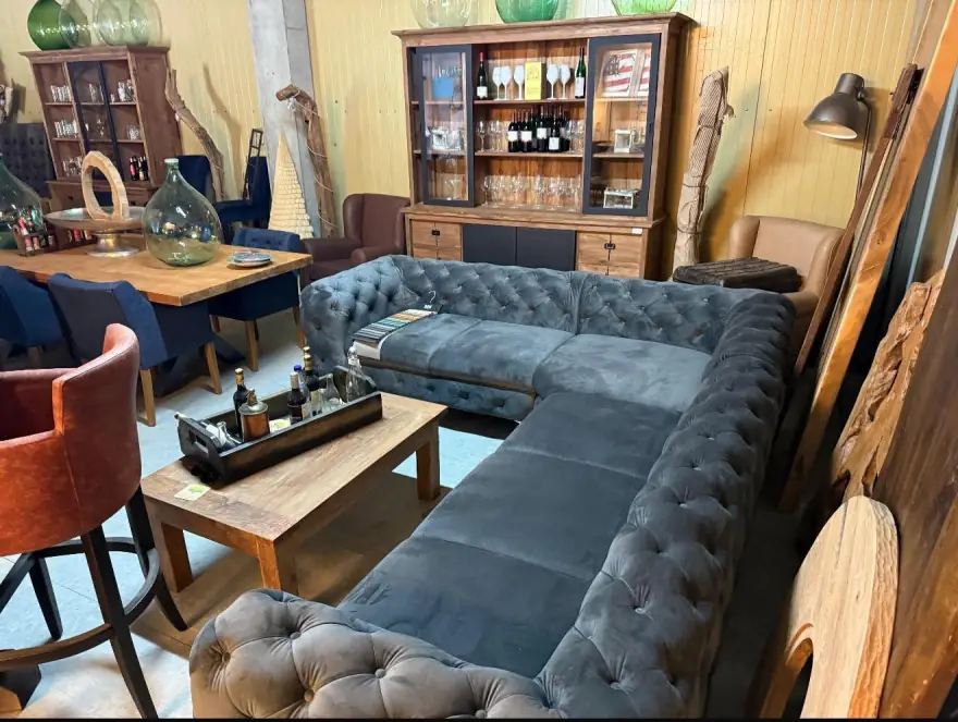 Blaues Chesterfield-Ecksofa mit Knopfheftung neben einem Massivholztisch